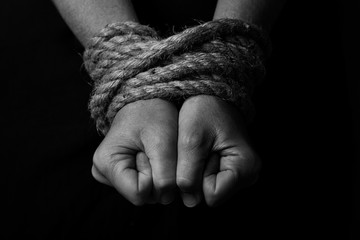 Conceptual monochrome image of woman hands tied with a coarse rope