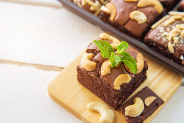 Fototapeta na wymiar Chocolate brownies with cashew nut and peppermint on wooden plate on white wooden floor with brownies box blurred background.