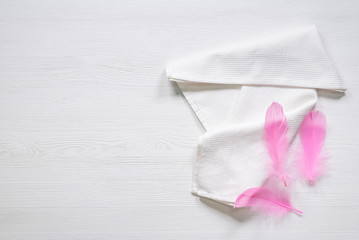 White towel and pink bird feather on a white wooden table background with copy space.