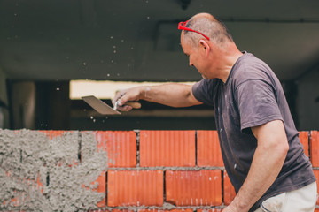 A man throwing cement on a brick wall of a home building. DIY home construction of a building -...
