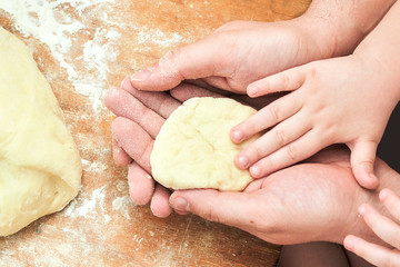 Dad and a small child in the kitchen are making dough. Joint creative work of the son and the father. Hands of a small child and dad close up
