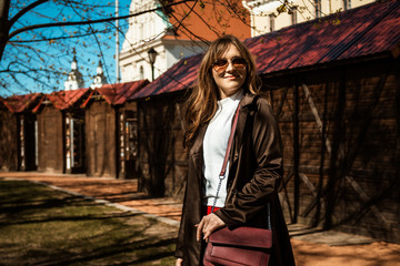 Outdoor portrait of young happy smiling fashionable lady wearing trendy red trousers, classic coat, holding red handbag, posing in street of European city.