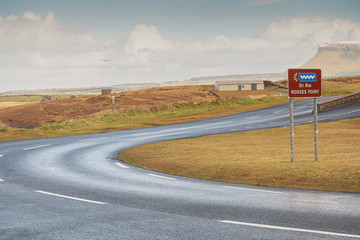 Rosses point road sign. Cloudy sky, road leads to  Benbulben topflat mountain covered with snow in the background. County Sligo, Ireland.