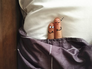Two fingers are decorated as two person. They are lying on bed. One of them is sleeping and another...