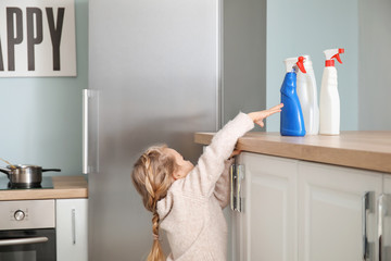 Little girl trying to reach out for bottles of detergent at home