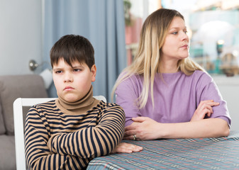 Offended son sitting at tablr after quarrel with mother at home