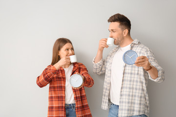Young couple with coffee and alarm clocks on light background