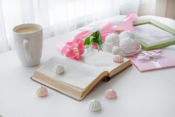 postcard good morning. Still life : a Cup of tea, a bouquet of pink tulips, a marshmallow book on a light background near the window.
