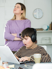 Son plaing video games at laptop, sad mom on background