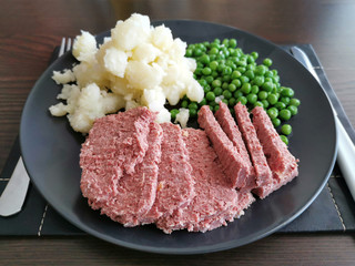 Corned beef with potato and peas on a black plate.  Selective focus at corned beef. 