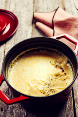 Creamy Polenta with baked onion and cheese in cast iron pot on rustic wooden background. Italian food. Selective focus. Toned image