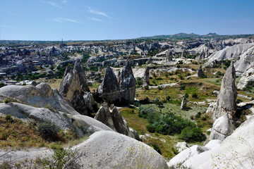 Valley of Cappadocia. Strange white cliffs with sharp peaks. The plain is covered with green grass. Blue sky with clouds.