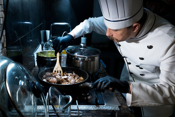 Chef cook in uniform cooks meat in a pan on the stove