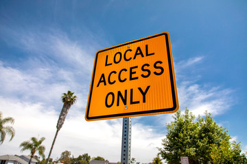 Yellow and black square road sign in neighborhood reading Local Access Only agasint a blue sky with...