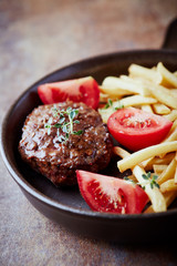 Hamburger steak with french fries and tomatoes. Brown stone background. Close up.	