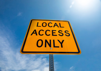 Yellow and black square road sign in neighborhood reading Local Access Only agasint a blue sky with...