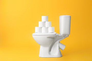 Toilet bowl with rolls of paper on color background