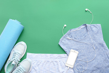 Sportswear, yoga mat and mobile phone on color background