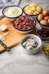 Zutaten  für Norddeutscher Hamburger Labskaus mit Rindfleisch Corned Beef, Rote Beete, Kartoffeln, Saure Gurken, Zwiebeln, Ei und Rollmops auf Marmor Arbeitsfläche