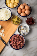 Zutaten  für Norddeutscher Hamburger Labskaus mit Rindfleisch Corned Beef, Rote Beete, Kartoffeln, Saure Gurken, Zwiebeln, Ei und Rollmops auf Marmor Arbeitsfläche