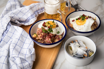 Norddeutscher Hamburger Labskaus mit Rindfleisch Corned Beef, Rote Beete, Kartoffeln, Saure Gurken, Spiegelei, Rollmops und Bier auf Marmor