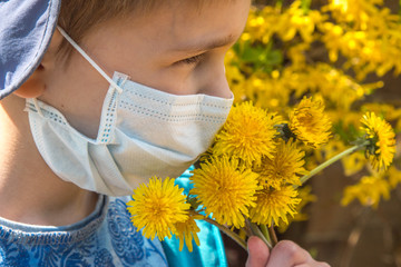 boy sniffing a dandelion in a protective medical mask