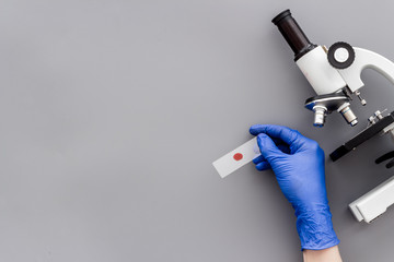 Clinical science research with microscope. Hand holds blood sample on grey background top view copy...