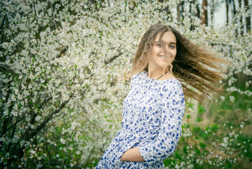 Fototapeta na wymiar Beautiful Girl with long hair in the spring. Girl teenager in the spring among the blooming garden. Happy girl in a blooming apricot garden. beautiful girl with wavy hair. Long hair in motion.