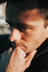 handsome brutal thin man with big brown eyes, clear skin, and rough stubble in a dark car and black clothes. bold portrait of a man close up. selective focus, mood toning