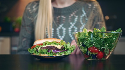 Close-up shot of Young lady preferring hamburger to salad. Attractive young woman choosing to eat healthy hamburger for breakfast.