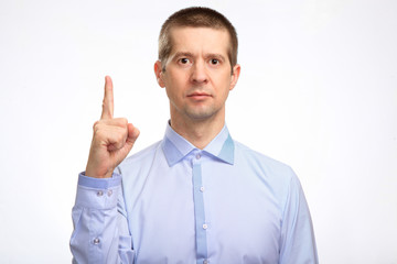 successful business man points his index finger in up, in a blue light casual shirt, looking into the camera. Isolated