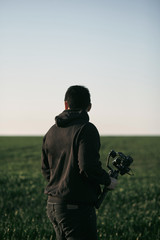 young male video operator standing in the green field with stabilization gimbal and camera © AlexGo