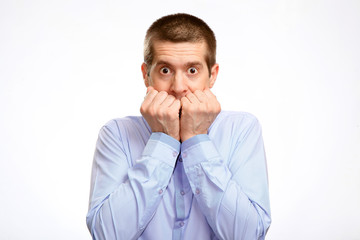 timid shy hesitant man pressed his fists to his lips, head, in a blue light casual shirt. Isolated