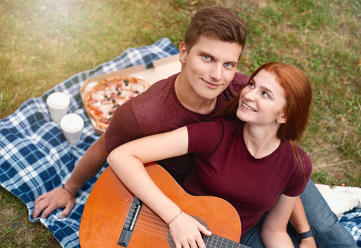 Happy couple in love on a romantic date at the park on a picnic. Playing on a guitar and having fun outdoors.