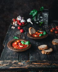 tomato soup in ceramic bowls with fresh basil leaves and bread slice on wooden background