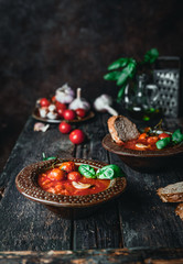 tomato soup in ceramic bowls with fresh basil leaves and bread slice on wooden background