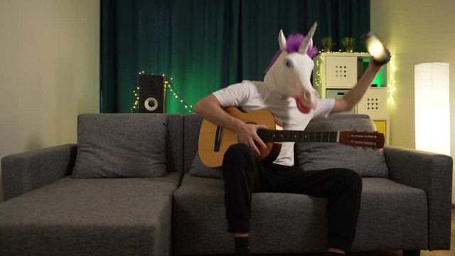 the man in the mask of a unicorn playing the guitar and dancing to the music