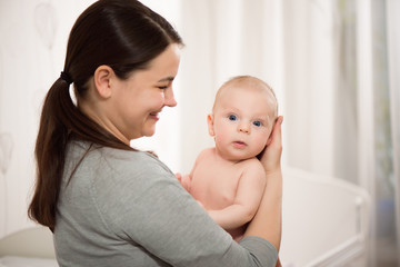 Young mother hugging her newborn child. Love, trust and tenderness concept. Bedding and textile for nursery.