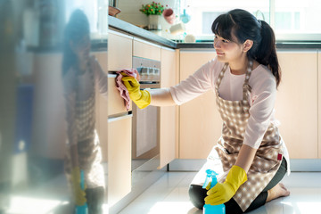 Asian woman wearing rubber protective gloves cleaning kitchen cupboards in her home during Staying at home using free time about their daily housekeeping routine.