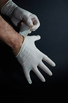 Par de manos humanas masculinas poni&eacute;ndose unos guantes de l&aacute;tex sobre un fondo negro