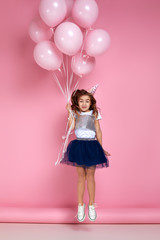 Obraz na płótnie Canvas Beautiful happy little child girl in dress and birthday hat jumping with pastel pink air balloons isolated on pink background. birthday party.