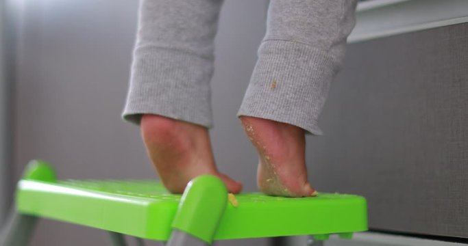 Baby standing on tiptoes reaching out, cute one year old infant on little chair tip-toe