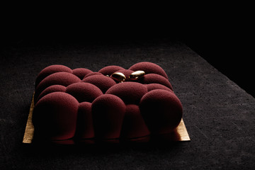 Embossed red mousse cake in the shape of bubbles and spheres with a Golden decor on a dark table. Low key. High confectionery skills