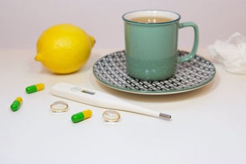 A cup of hot herbal tea with lemon; thermometer, pills and paper wipes as a treatment and health care concept during a flu and virus fever.