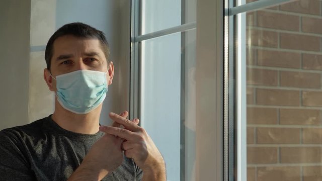 Concept home quarantine, prevention COVID-19. Forced Home Isolation. Sick man with mask is quarantined at home and looks out the window sadly. He cannot get out due to the COVID19 coronavirus pandemic