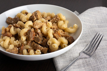 Pasta with meat and sesame in a plate next to a fork and napkin.