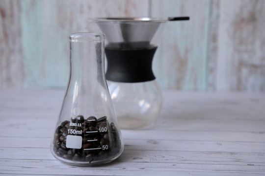 Coffee beans in a glass measuring flask and a coffee maker are on the table