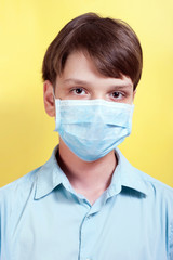 A beautiful boy with a blue medical mask on a yellow background. Concept protection from viruses, seasonal respiratory diseases, flu, coronavirus, COVID-19.