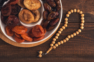 top view plate of dried fruit, wooden rosary on brown wooden background, iftar concept, Ramadan