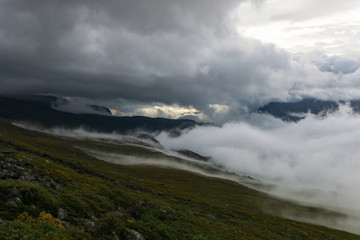 Fototapeta na wymiar Morning mist is rising towards the peaks of the Laddjuvaggi valley slopes in Sweden Lapland